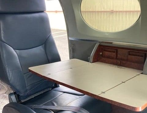 A gray leather seat with a fold-out table in the aircraft cabin.