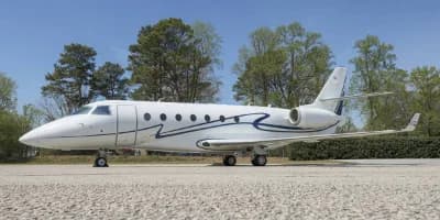 A white Gulfstream G280 parked on a gravel surface.
