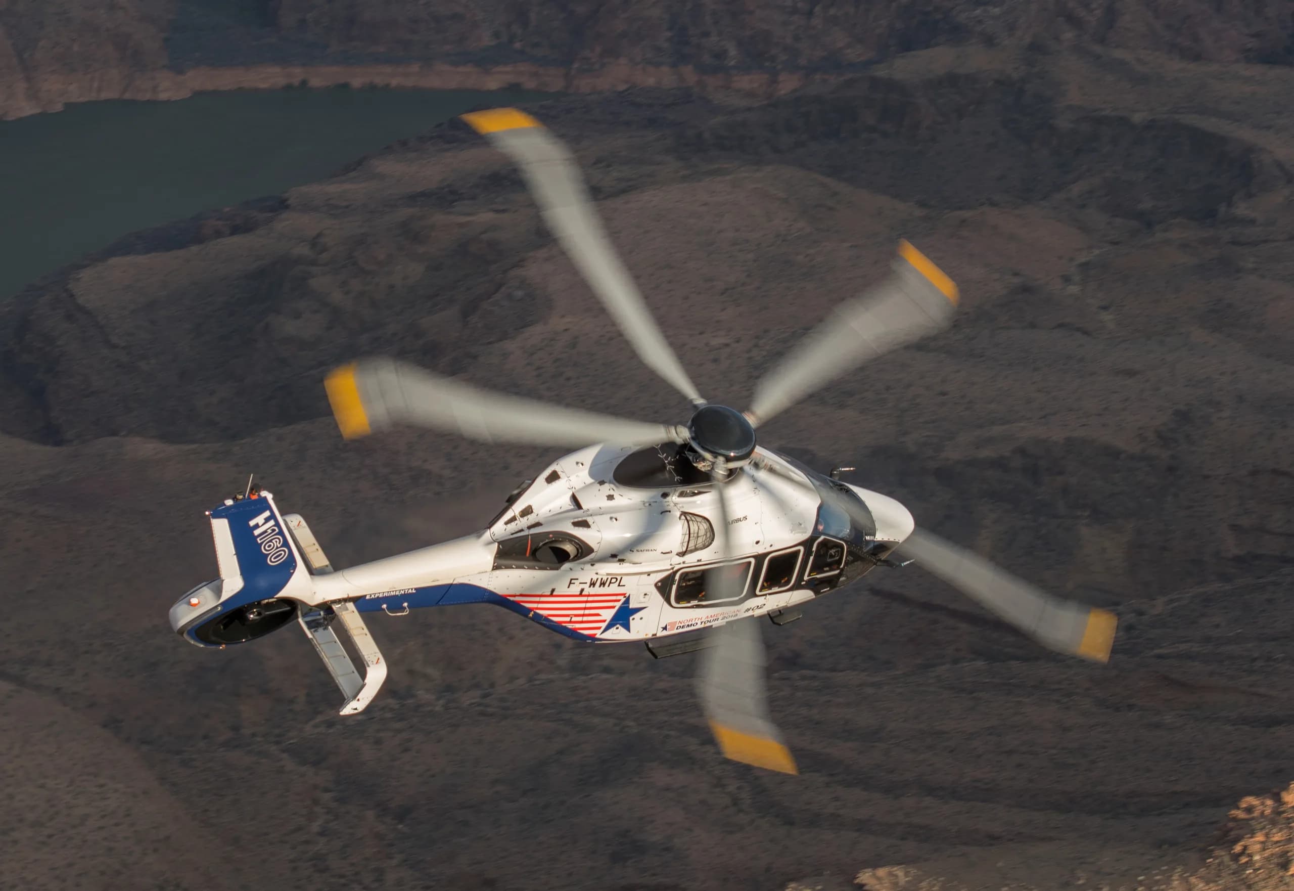An Airbus H160 helicopter flying over a desert landscape.