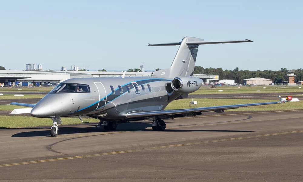 Front side view of a silver and blue Embraer Phenom 300 with registration VH-PIL on the tarmac.