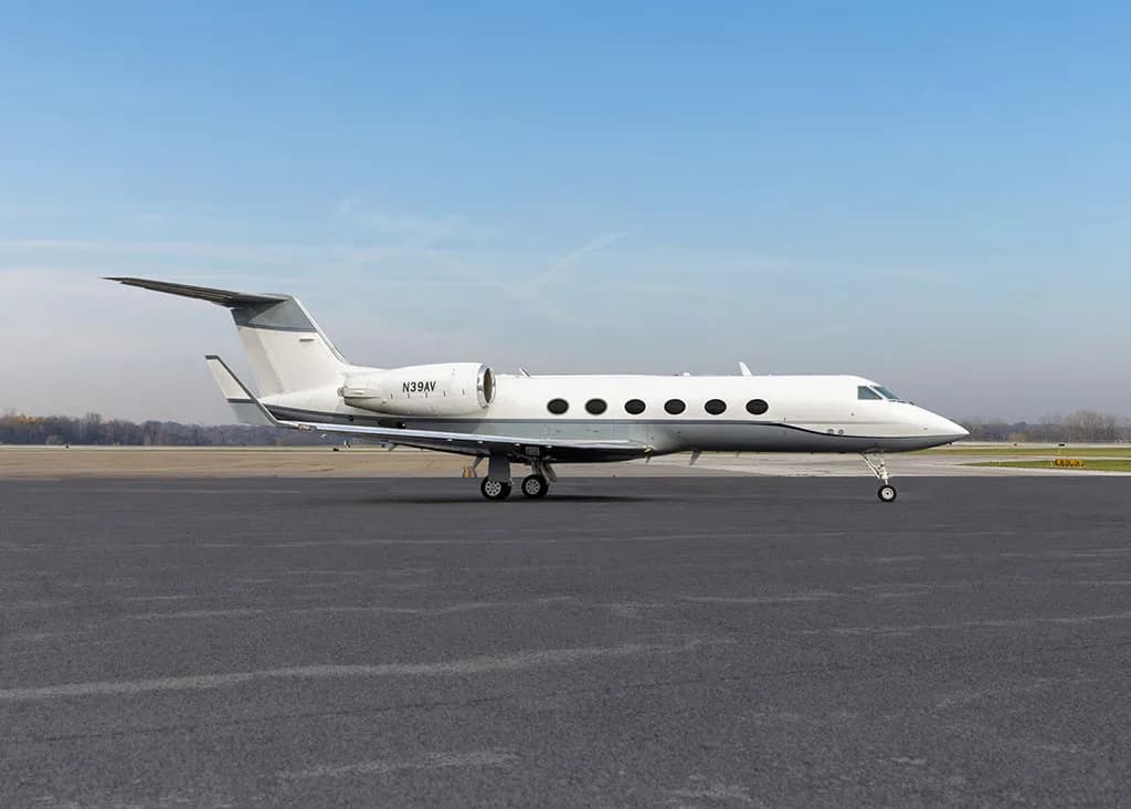 A white Gulfstream G550 aircraft (N39AV) is parked on a tarmac, viewed from the front-side.