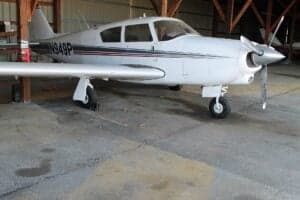 A white single-engine propeller aircraft with red and black stripes, parked inside a hangar.