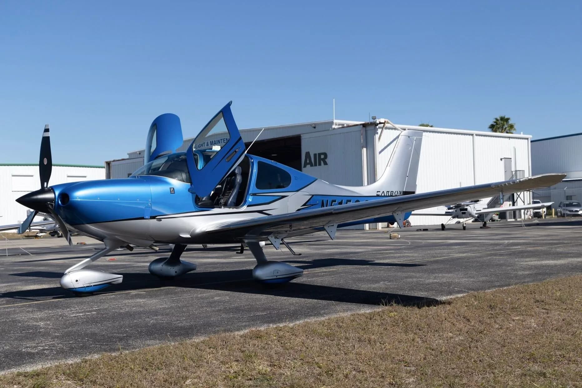 A blue and silver Cirrus SR22 aircraft (N515SC) with its doors open, parked on an airfield.