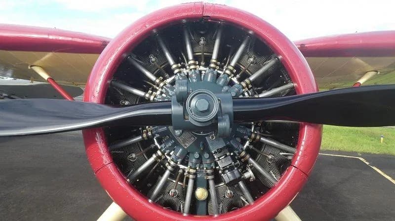 A close-up view of the radial engine and propeller of a vintage aircraft, with a red cowling.