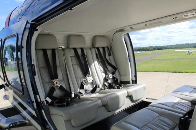 The interior of the helicopter with grey leather seats and black seatbelts.