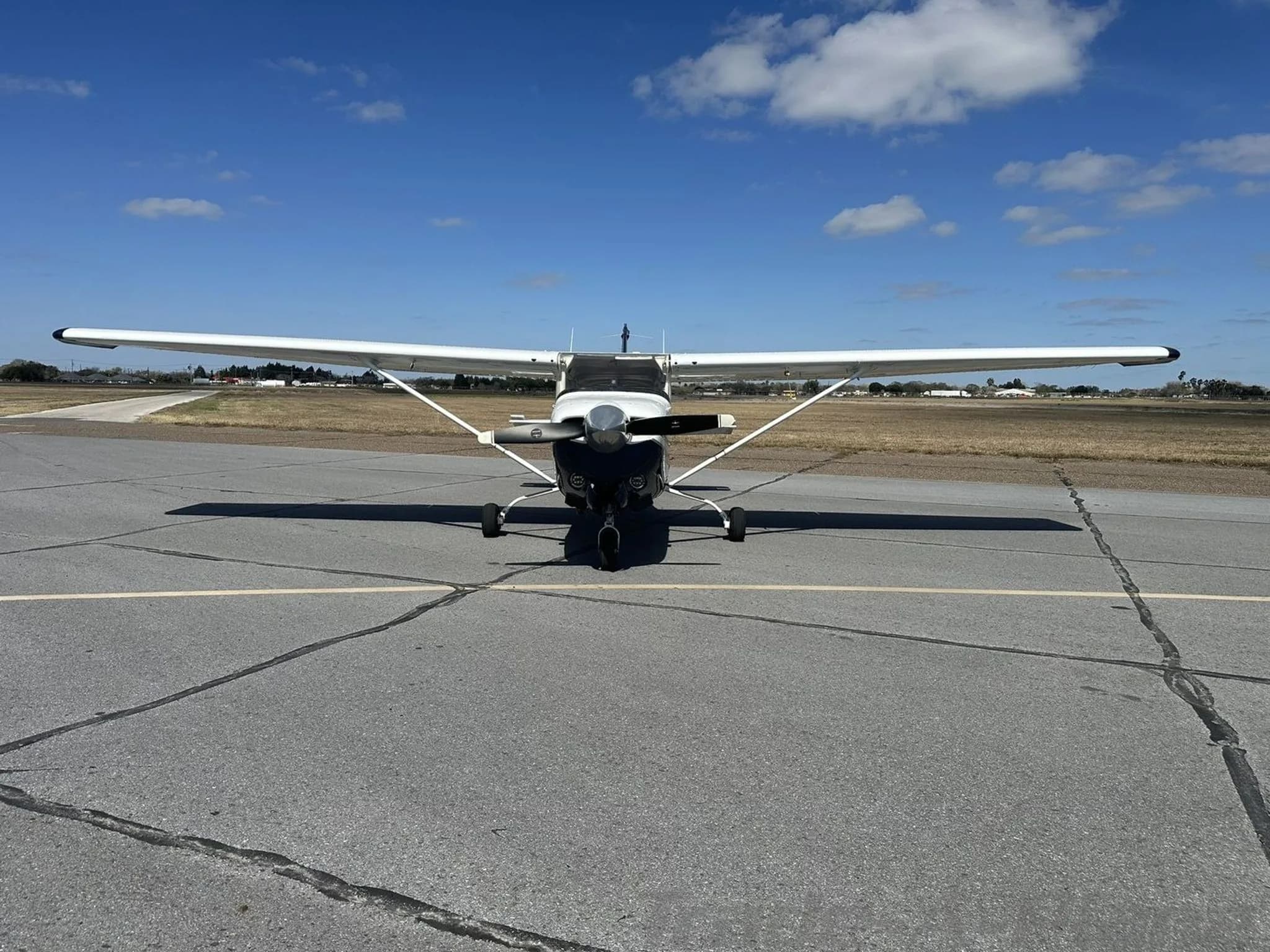 Front view of a white and dark blue Cessna aircraft N108EA parked on an airport tarmac under a blue sky.
