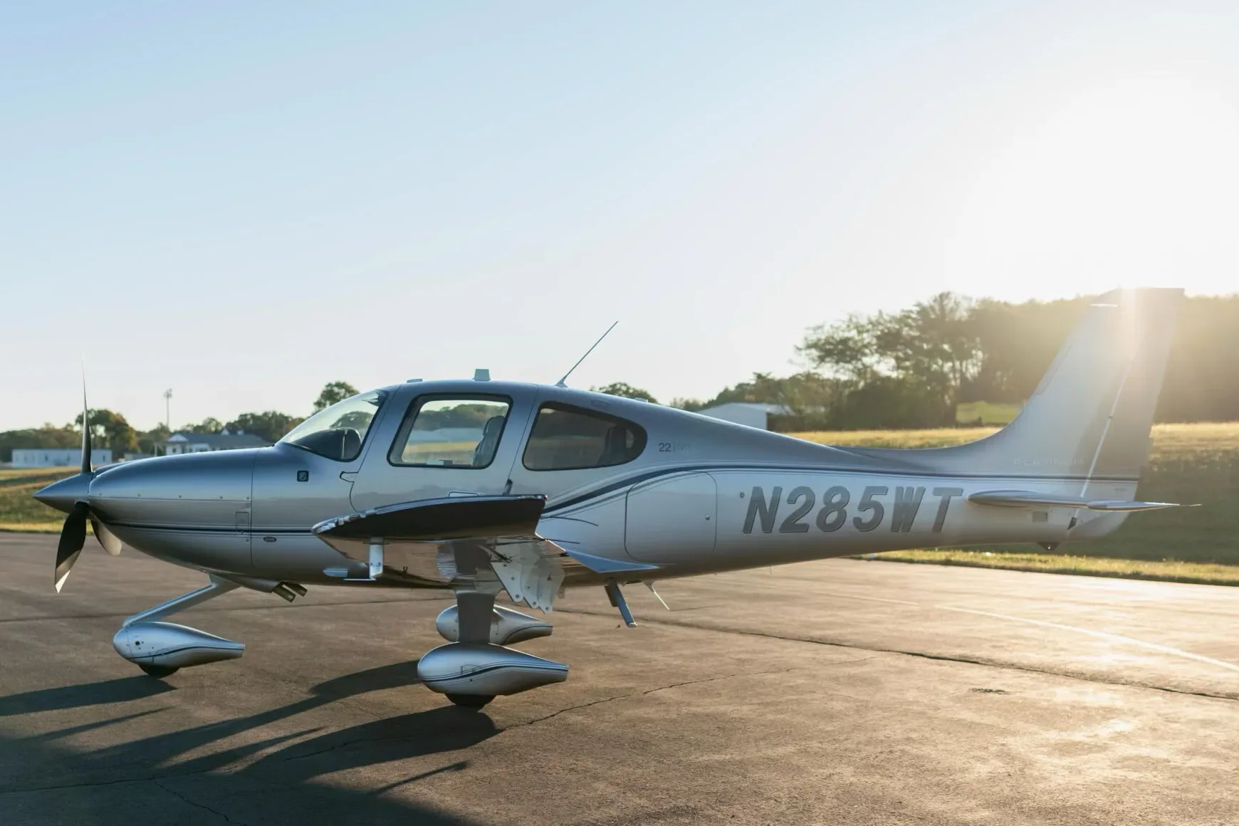 A side view of the silver and grey Cirrus SR22 aircraft (N285WT) with sun glare on the tail.