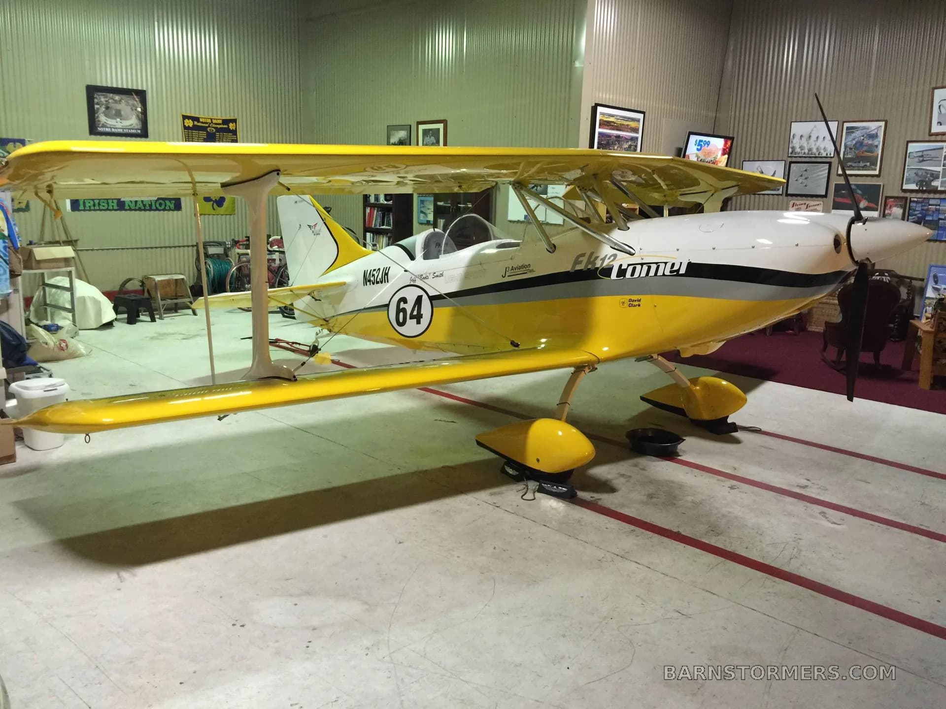 A yellow and white FK12 Comet biplane with '64' on the tail, parked in a hangar.