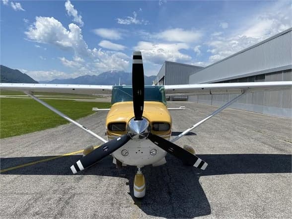 Close-up front view of a Cessna 210 Centurion aircraft on the tarmac in front of a hangar.