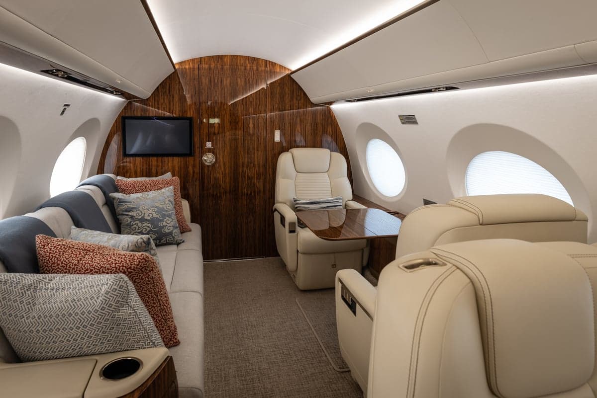 The interior of the aircraft features a sofa, chairs, and wood accents.