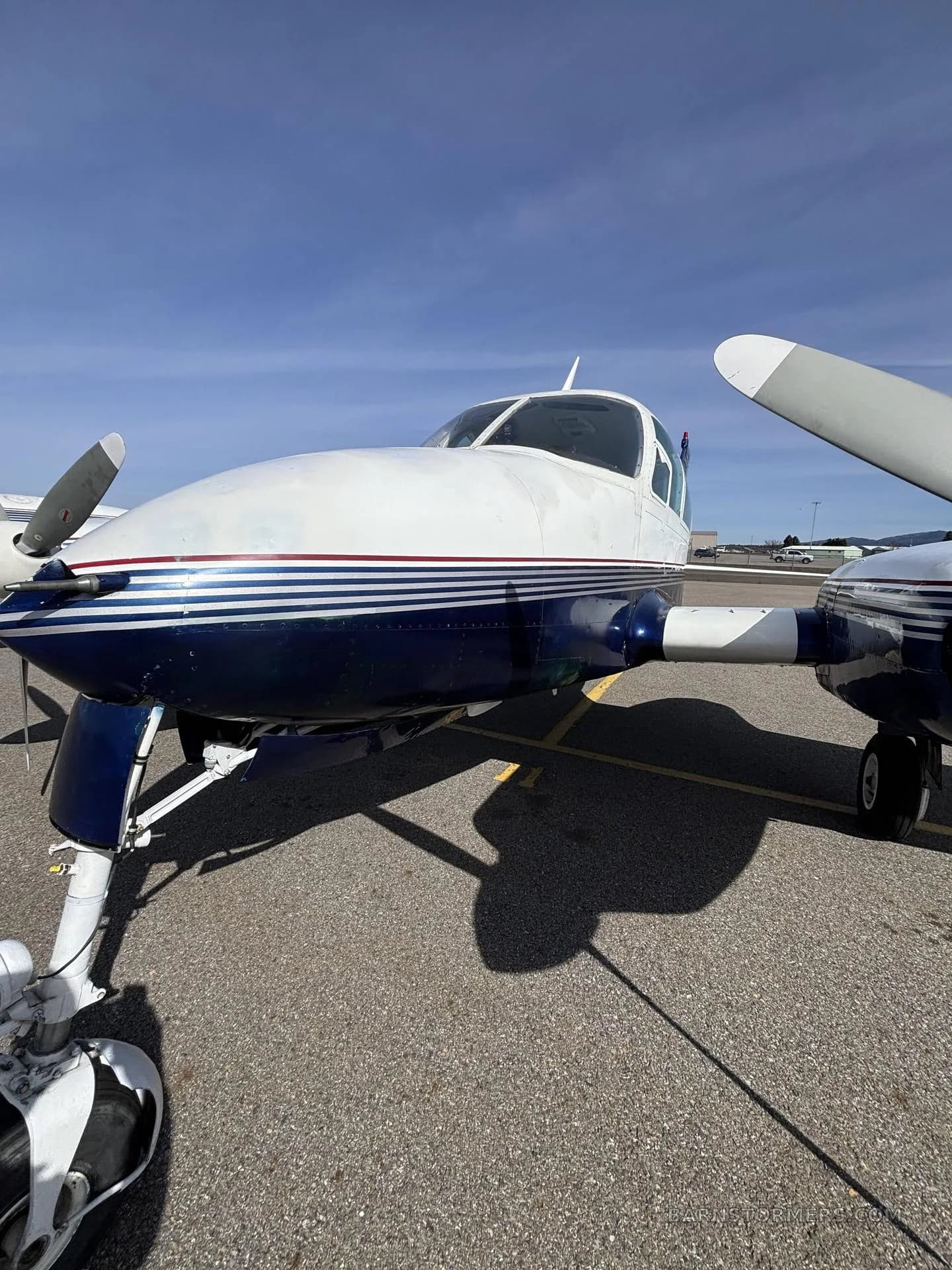 A close-up, low-angle view of the front of a white and blue Cessna 310I, registration N27ZZ, parked on an airfield.