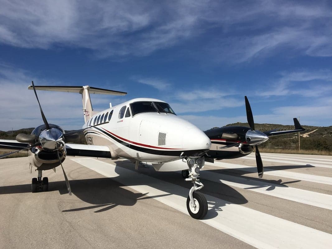 A King Air aircraft is parked on the runway with a blue sky background.