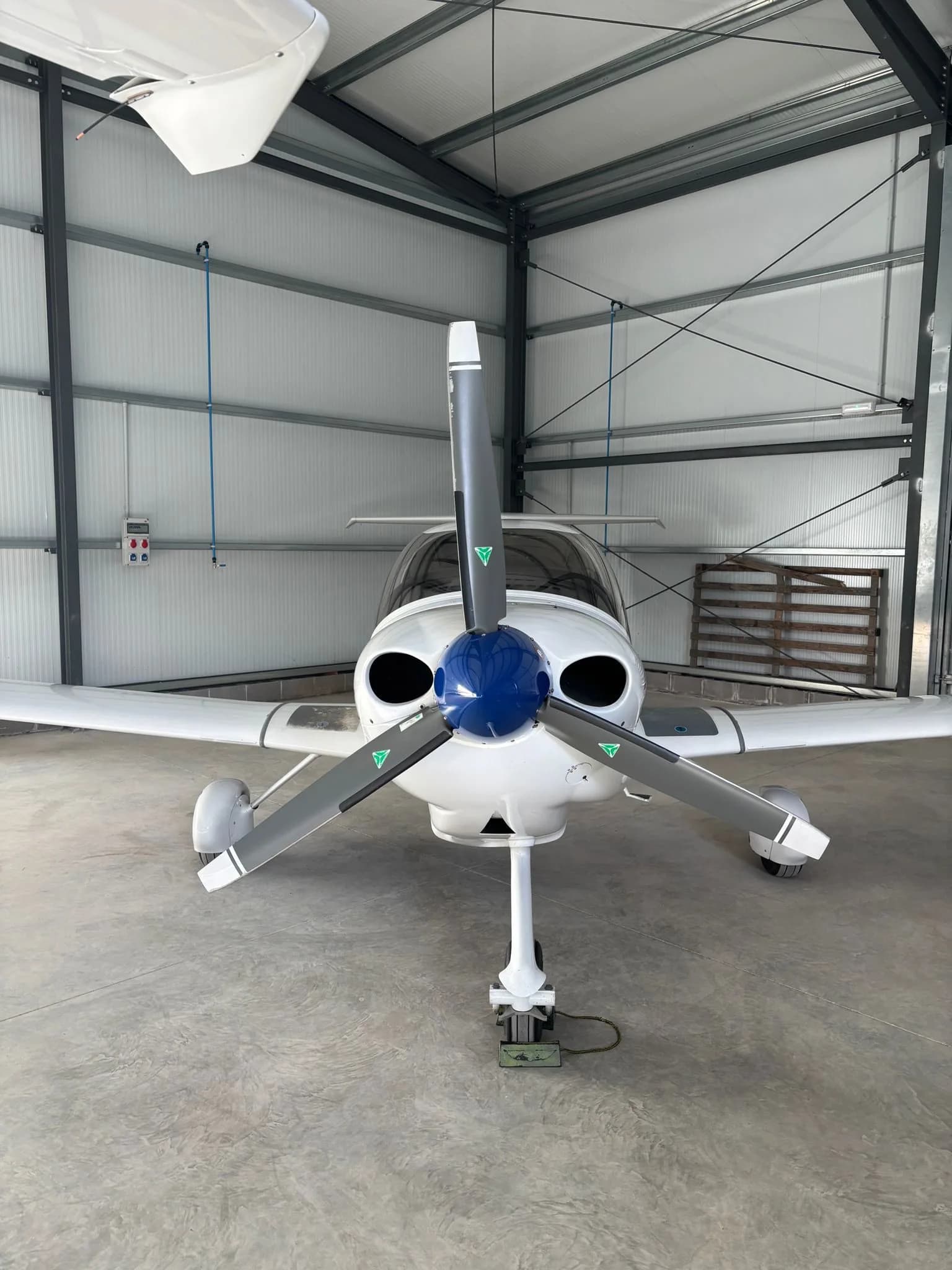 Front view of a white Diamond DA40 aircraft with a blue propeller hub inside a hangar.
