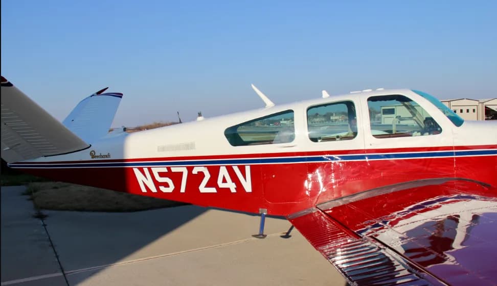 A close-up side view of the fuselage and tail of a red and white Beechcraft Bonanza N5724V.