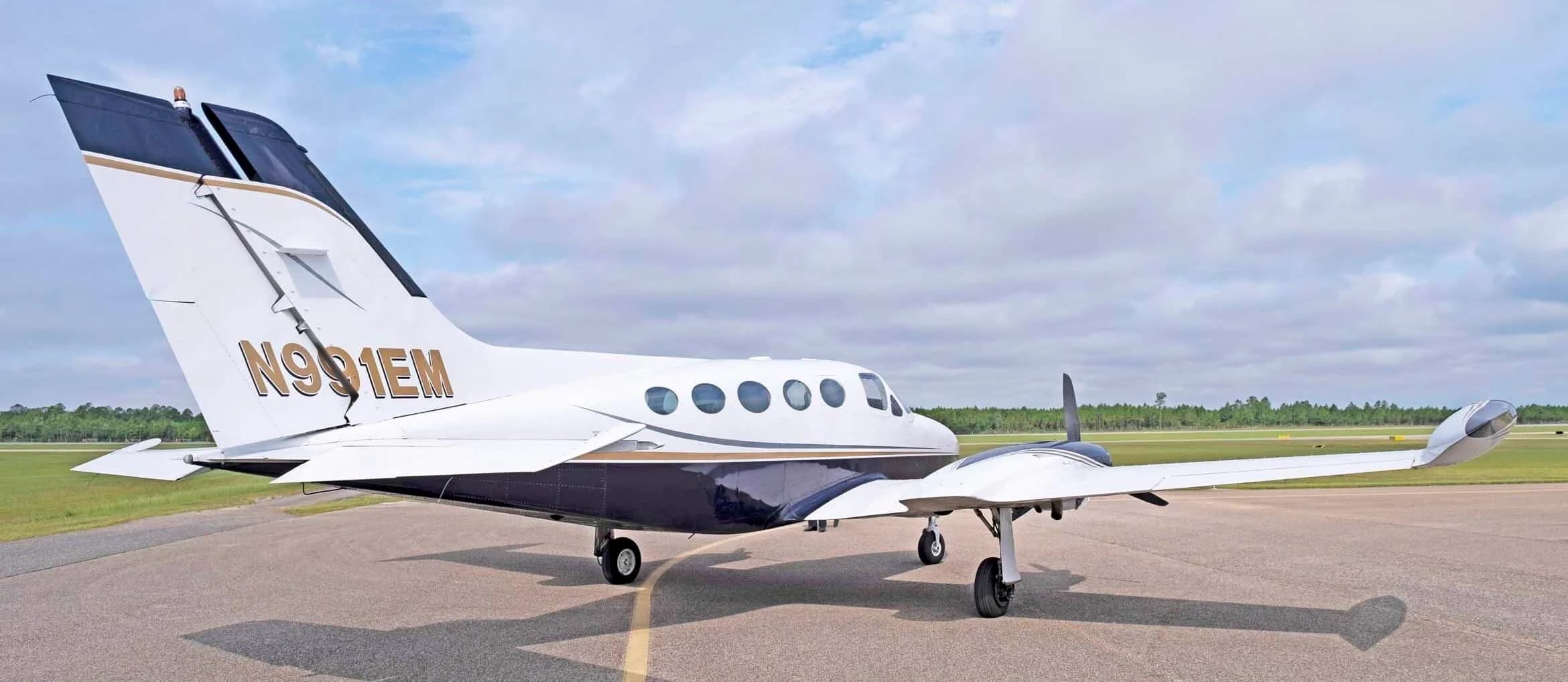 A rear-quarter view of the white and dark blue Cessna 414 Chancellor, registration N991EM, parked on an airfield.