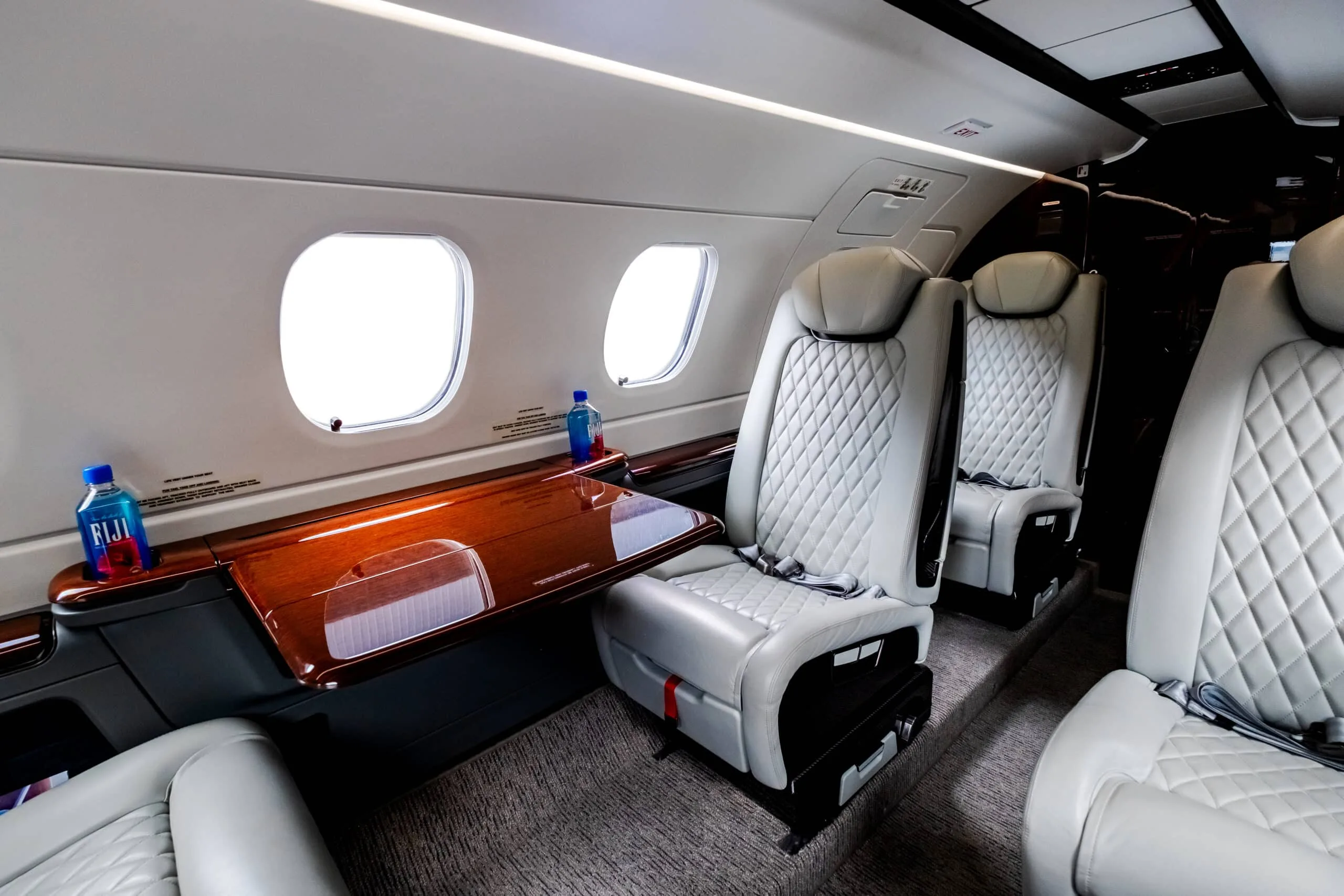 View of the aircraft cabin with white leather seats and wood table.