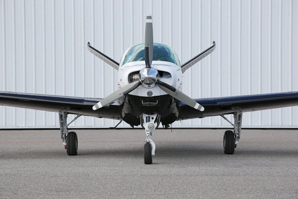 Very close-up front view of a Beechcraft Bonanza aircraft on the ground in front of a hangar.