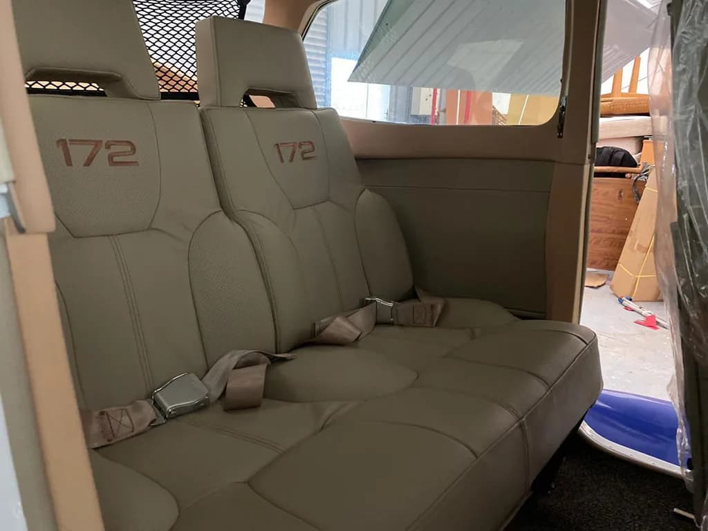 A close-up view of the tan rear seats in a Cessna 172 aircraft cabin, each embroidered with "172".