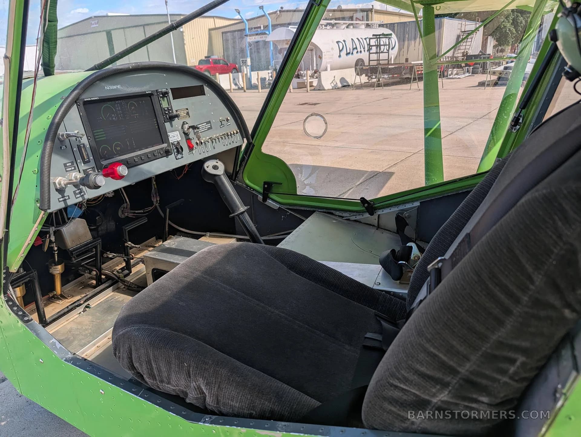 The interior of the green aircraft, showing the pilot's seat, instrument panel, and view out the side window.