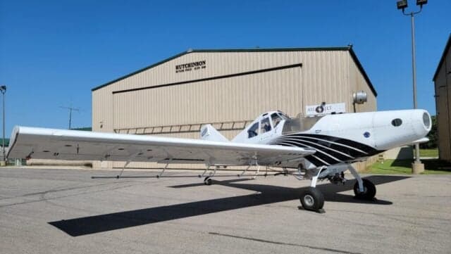 Full right side view of a white Thrush agricultural aircraft with black stripes, parked in front of a hangar.