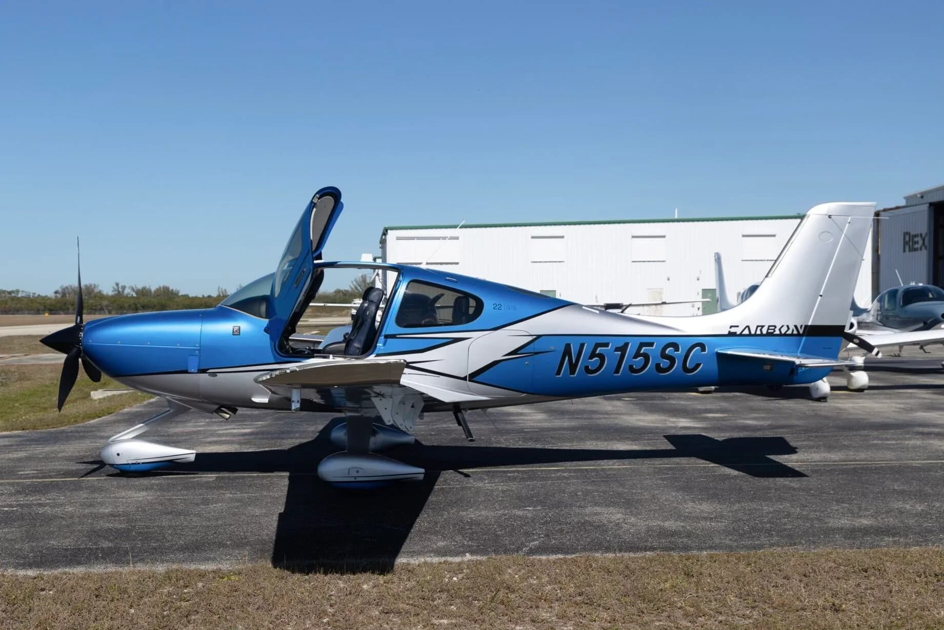 A side view of a blue and silver Cirrus SR22 aircraft (N515SC) with its doors open, parked on an airfield.