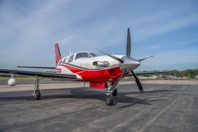 A front-quarter view of the white and red Piper M-class aircraft N555GP with its propeller, parked on an asphalt ramp.