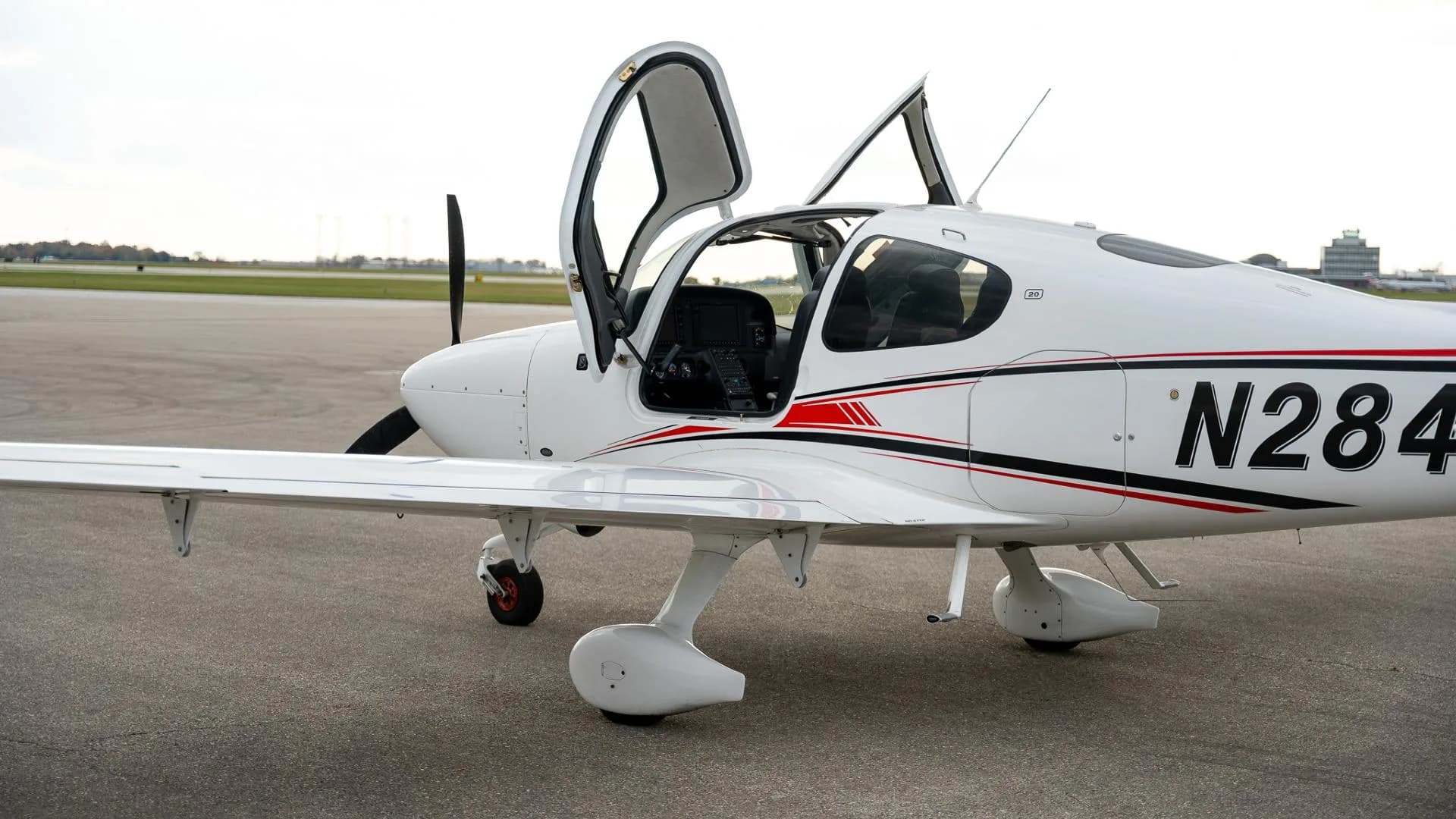 A side view of the white Cirrus SR22 aircraft with both doors open, revealing the cockpit interior.