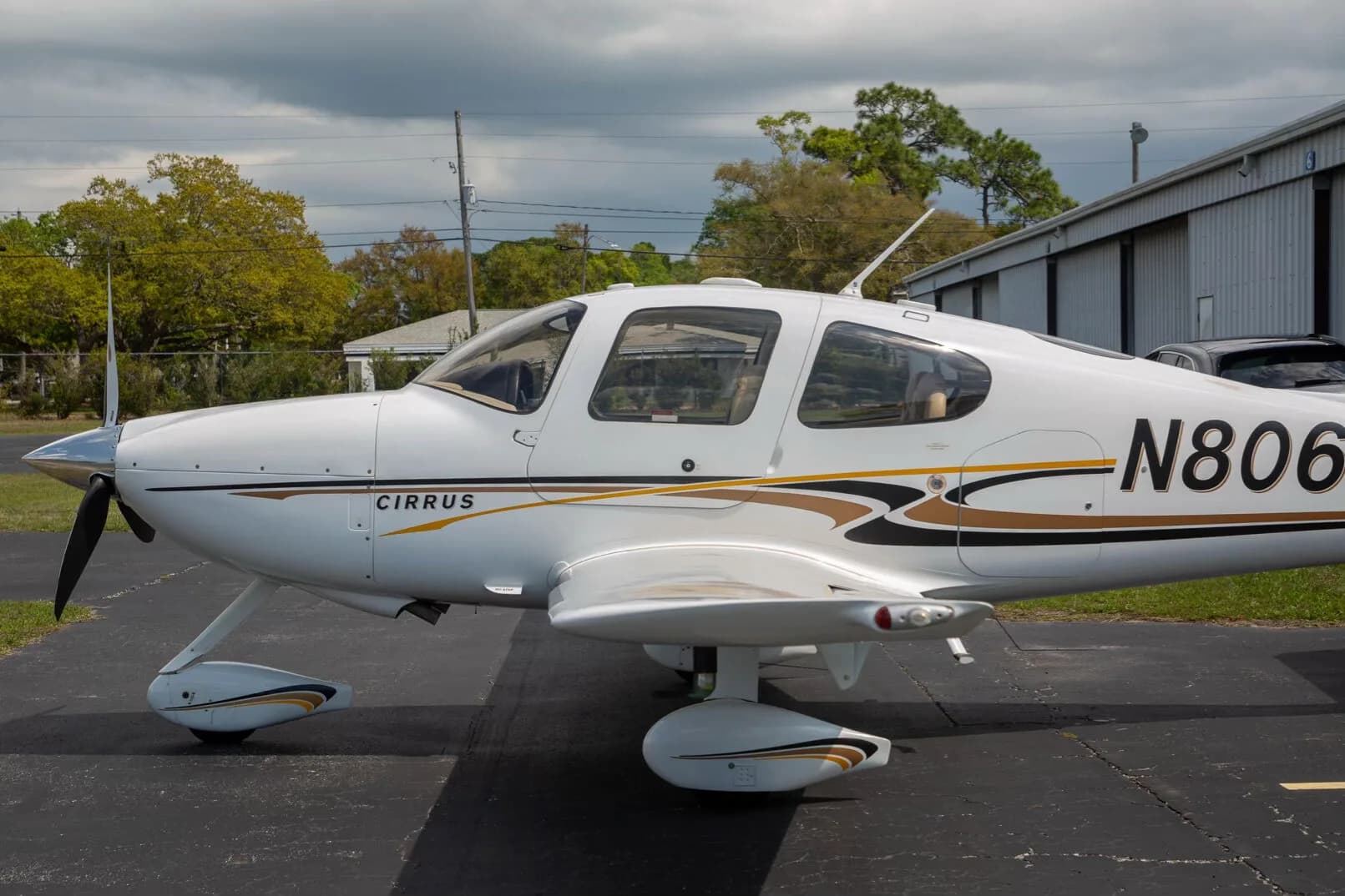 A close-up side view of the front fuselage of a white Cirrus SR22 aircraft with black and gold stripes.