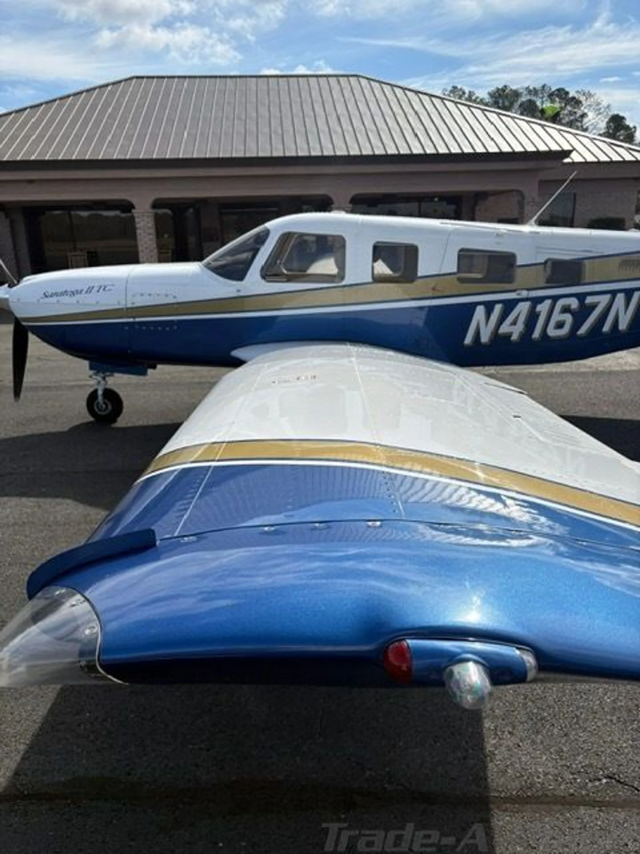 A close-up view of the right wing and fuselage of the Piper Saratoga II TC, N4167N, showing its white, blue, and gold paint scheme.