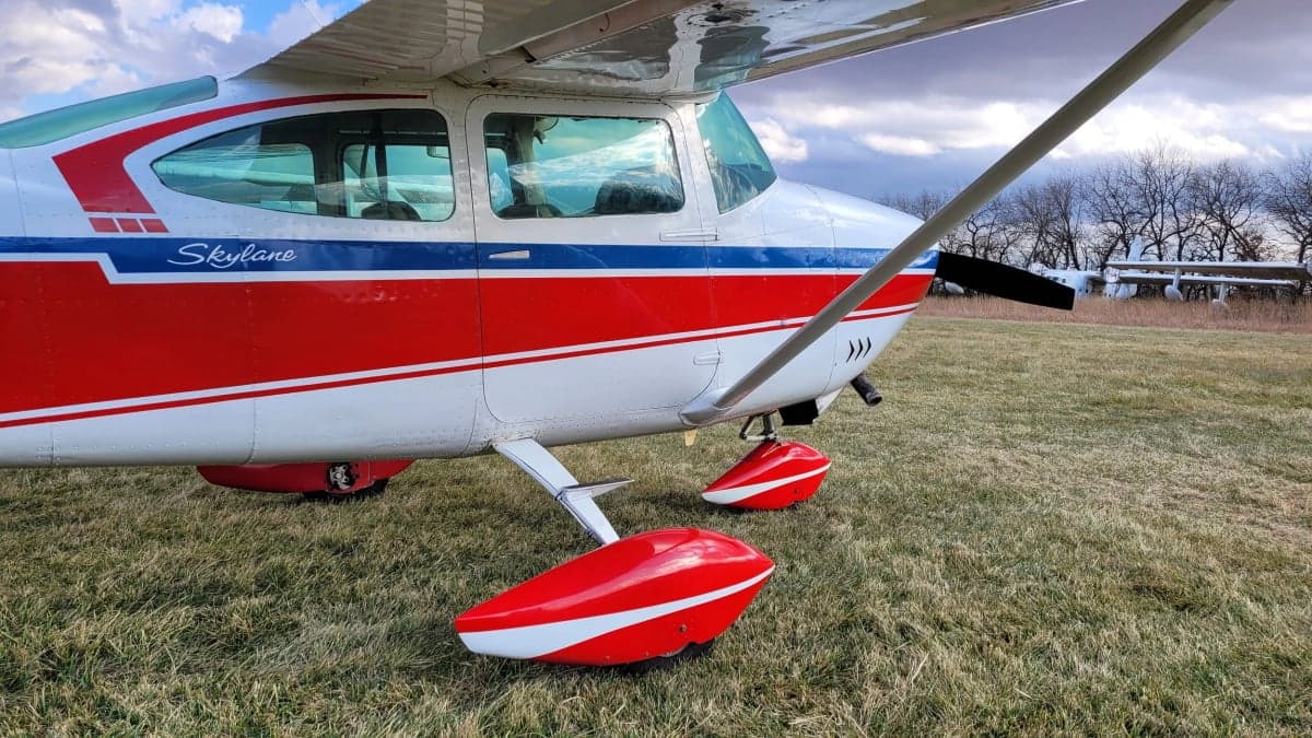 A close-up of the front of the Cessna Skylane with red, white, and blue paint scheme on a grassy field.