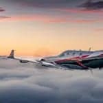 A white and red turboprop aircraft flies above the clouds during sunset.