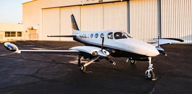 A twin-engine aircraft is parked on the tarmac in front of a hangar.