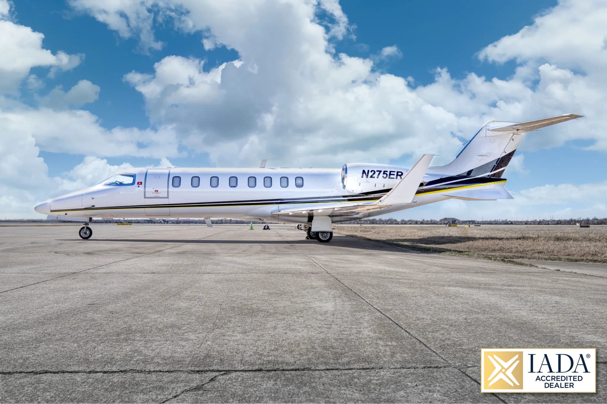 A side view of a white Learjet 60 (N275ER) with a black and yellow stripe, parked on a tarmac.