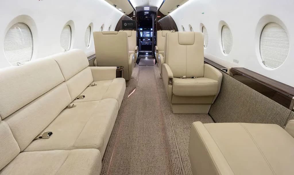 The spacious interior of the Gulfstream G550 cabin features a long beige sofa and individual cream-colored seats.