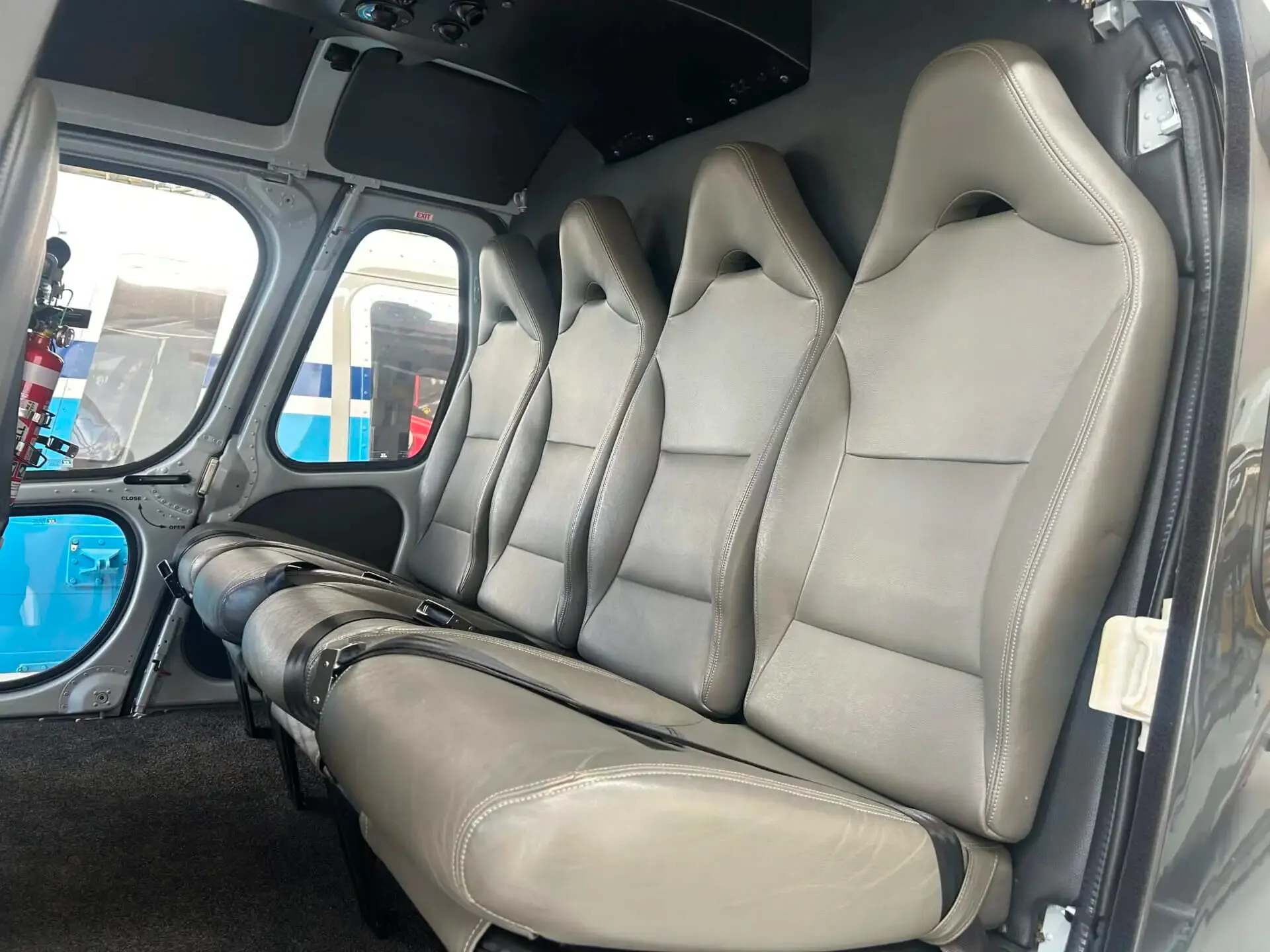 The grey leather passenger seats inside the cabin of a helicopter, viewed from the rear.