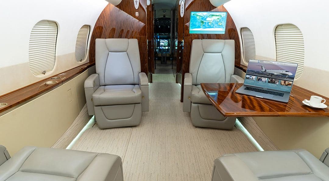 A view of the aircraft's interior, showing leather seats, wood trim, and a laptop on a table.