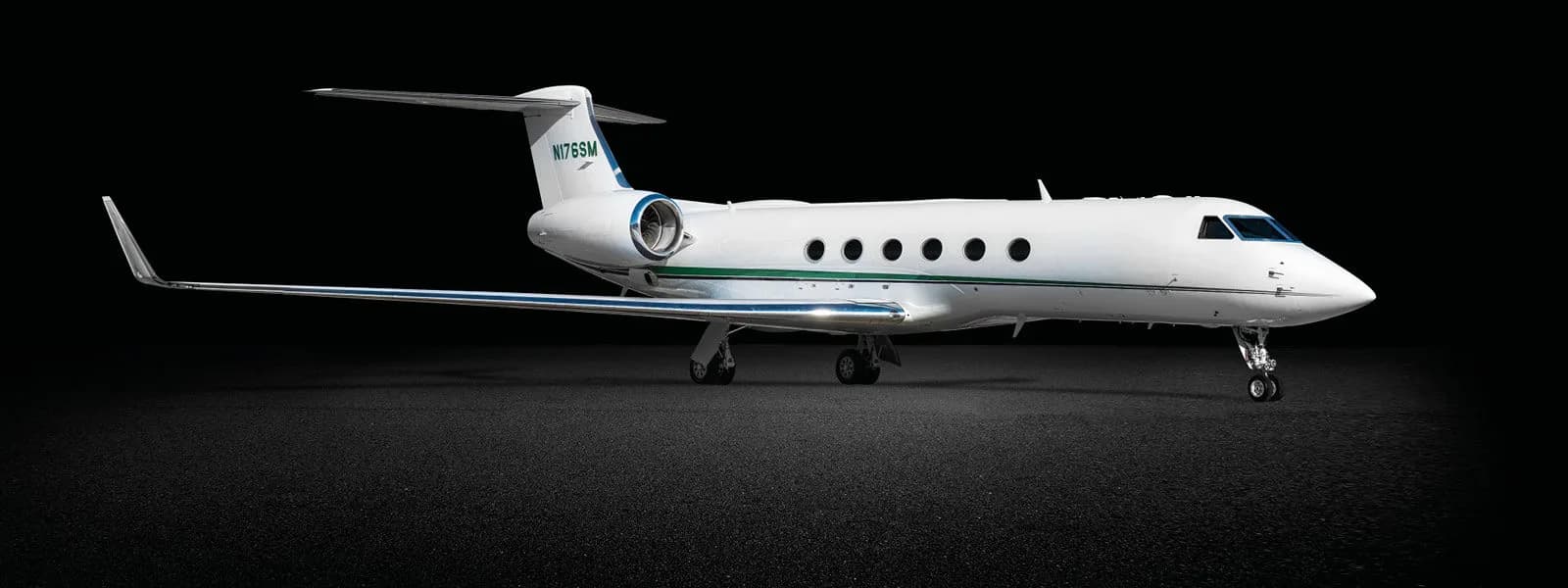 A white Gulfstream business jet with green accent stripes and registration N176SM on the tail, shown against a dark background.