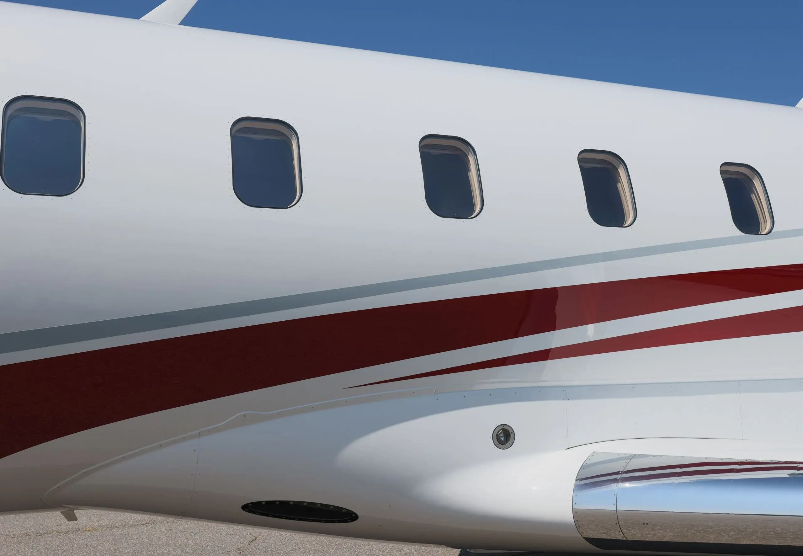 Close-up view of the fuselage windows and red and grey stripe detail on a white business jet.