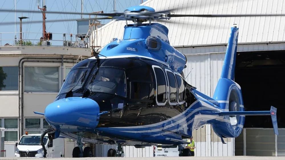 A blue and black Airbus H155 helicopter with a white stripe paint scheme on an airfield.