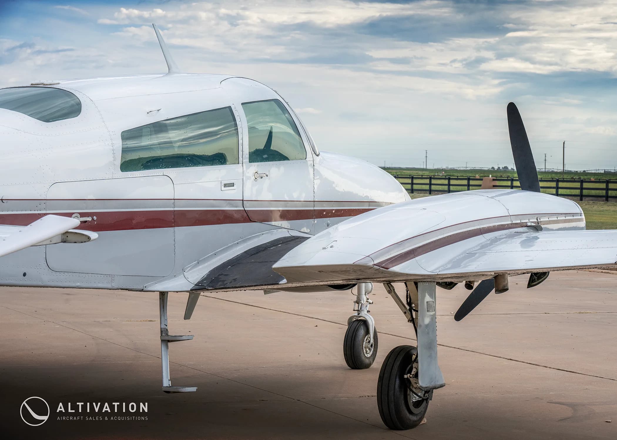 A close-up side view of the fuselage and left engine of a white twin-engine propeller aircraft with maroon stripes.