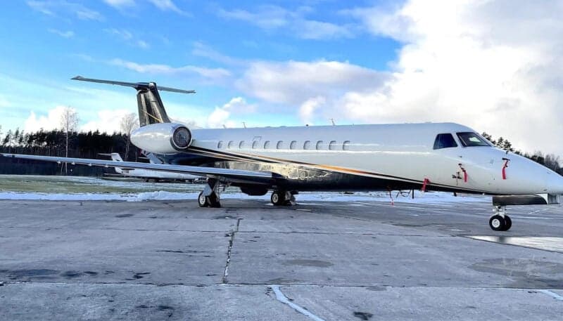 A white private jet with black and gold accents is parked on a snowy tarmac under a cloudy sky.