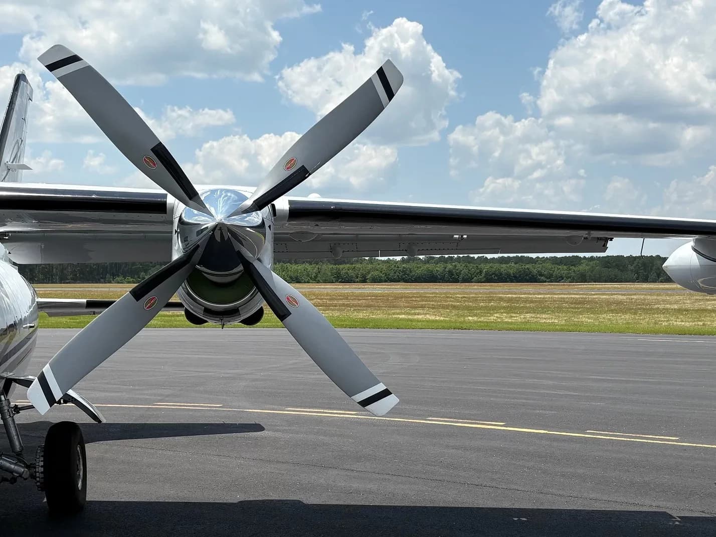 Close-up of the four-blade propeller and engine nacelle of a white aircraft on an airfield.