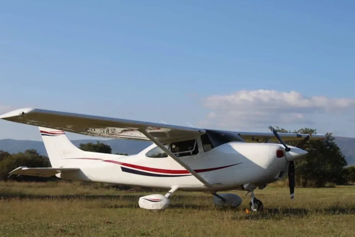 A Cessna aircraft is parked on a grassy field, showcasing its white paint scheme with red and blue accents.
