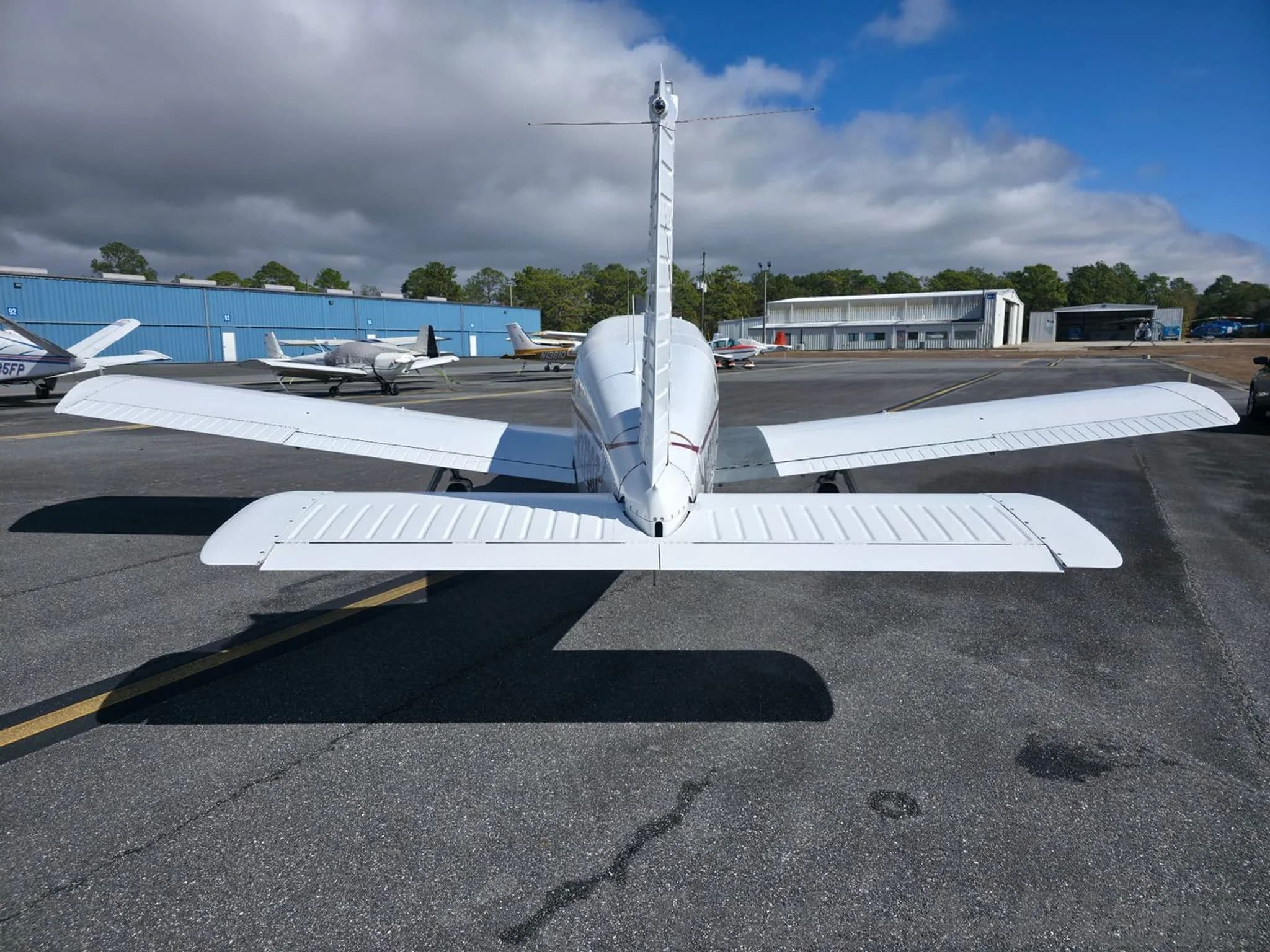 A rear view of the white Piper Arrow N3720T showing the tail and horizontal stabilizer, parked on an airfield.