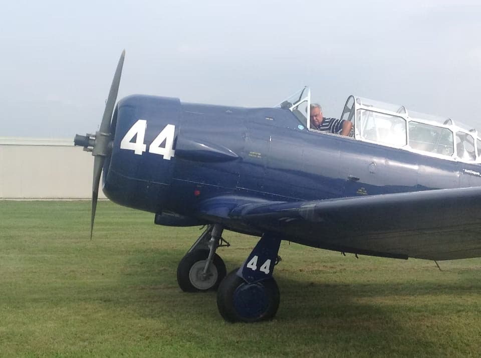 A blue North American T-6 Texan aircraft in flight, viewed from below.