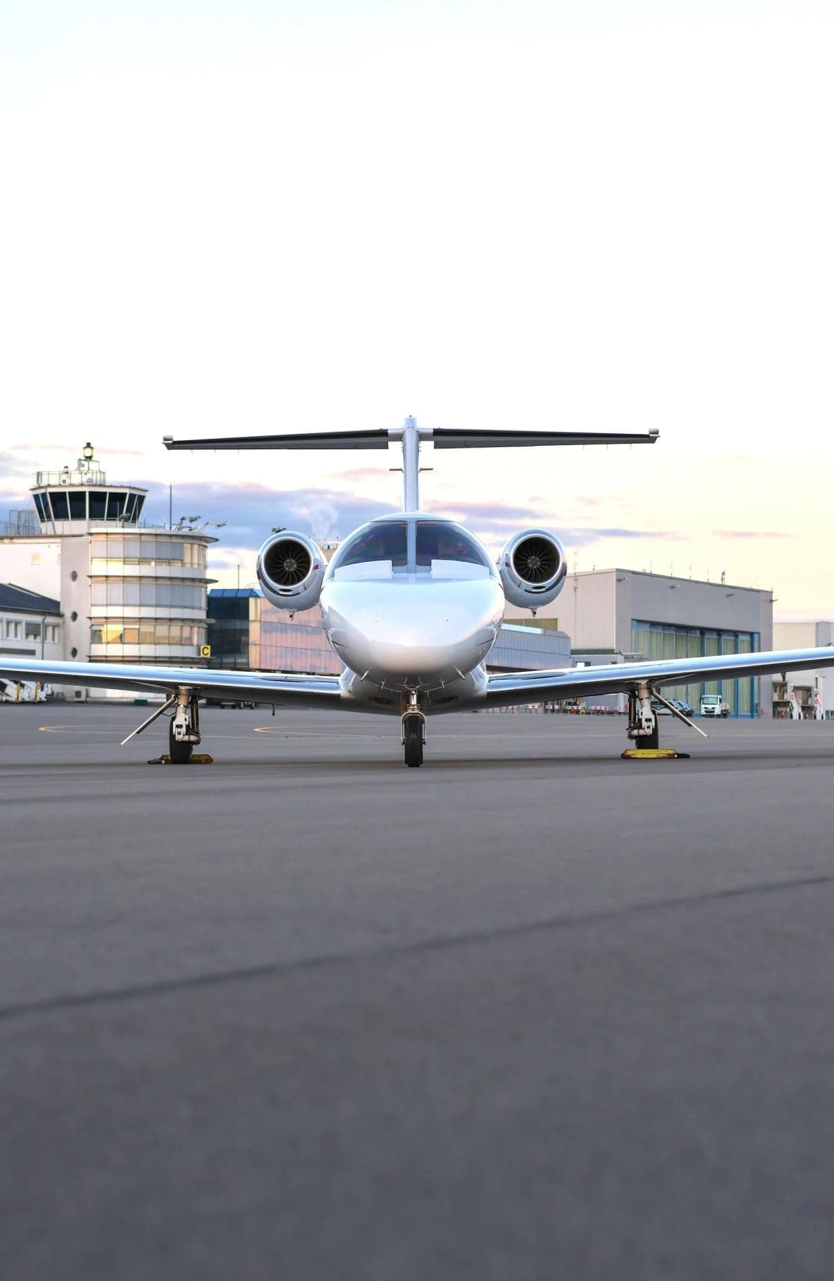Front view of a Cessna Citation CJ1+ aircraft on the tarmac with a control tower in the background.