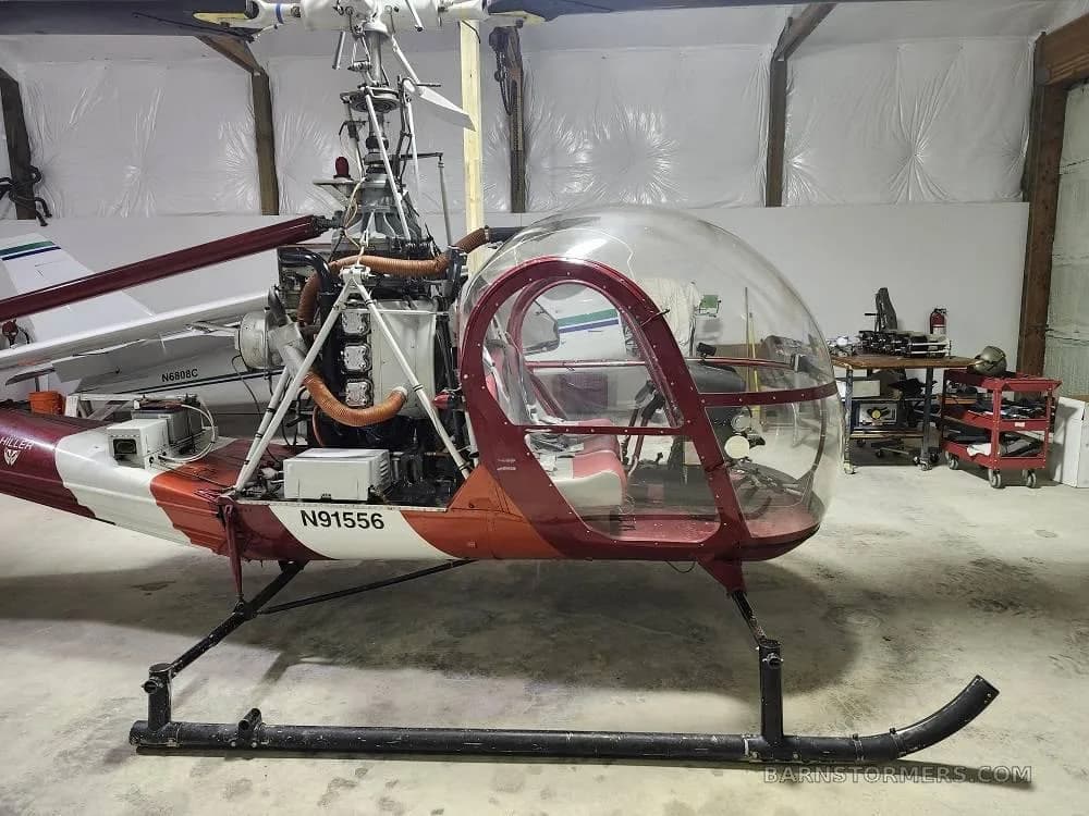 A red and white helicopter, N91556, with its engine exposed, is parked in a hangar.