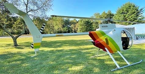 A side view of the N500ZK helicopter with a rainbow paint scheme on the tail, parked on grass.