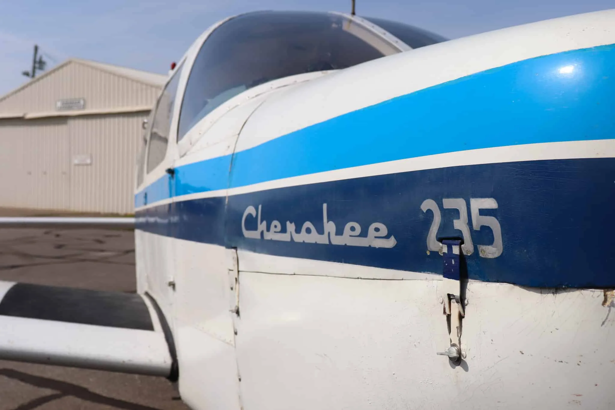 A close-up view of the "Cherokee 235" text and blue stripe on the side of the white aircraft fuselage.