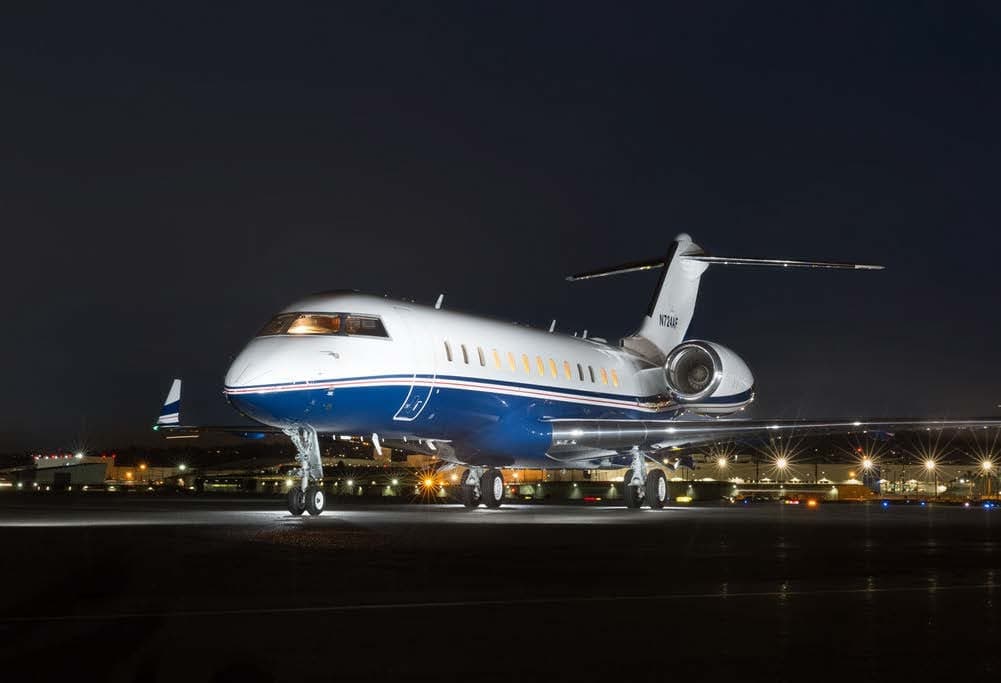 A Bombardier Challenger 300 aircraft is parked on the tarmac at night.